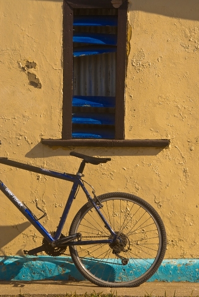 A bicycle leans up against a yellow stucco house with teal trim.