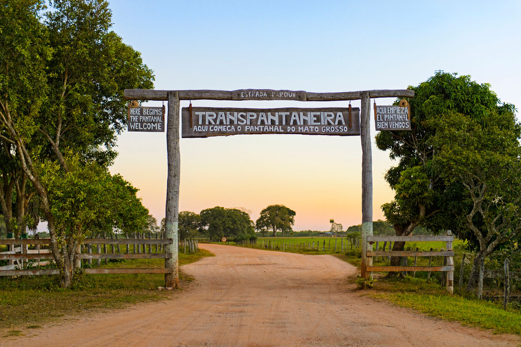 Hanging over a packed dirt road, a wooden sign in english and portguese which reads Transpantaneira and welcomes visitors.