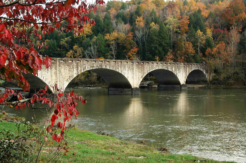 A stone bridge spanning a river with fall foliage on the banks.