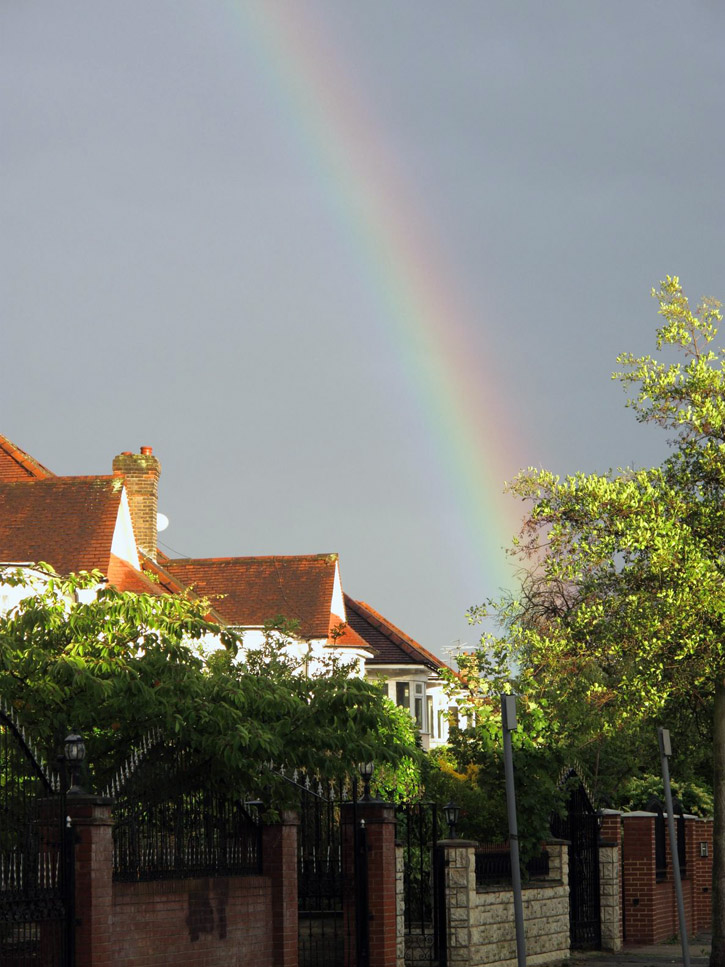 Rainbow with a dark overcast sky above suburban houses in London, England.