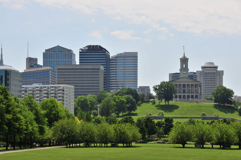 View across a well-maintained city park with the skyline and capitol building visible in the distance.