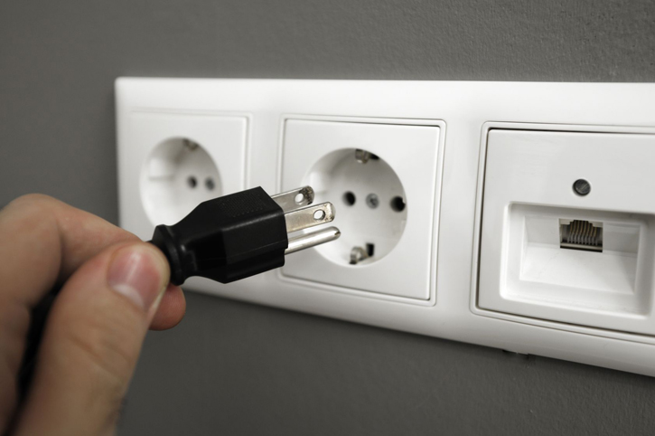An American plug is held up against a European wall socket.